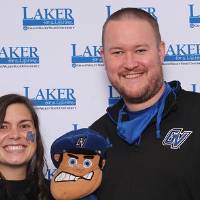 Two alumni holding up Louie the Laker puppet
